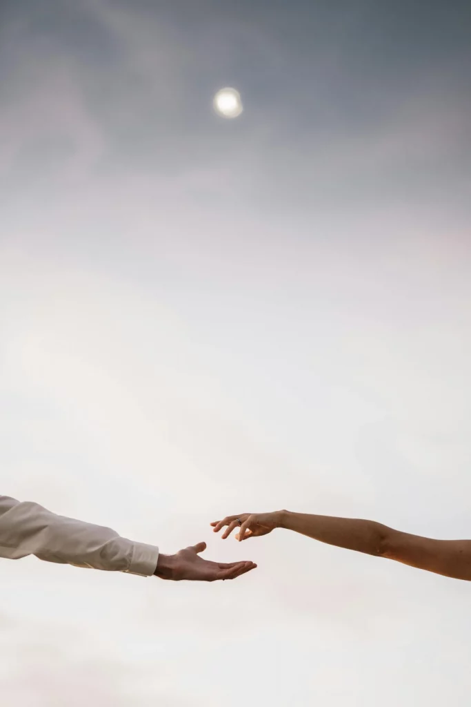 Zwei ausgestreckte Hände nähern sich vor einem ruhigen Himmel an – Symbol für Vertrauen, emotionale Verbundenheit, Annäherung und Beziehungsgestaltung.