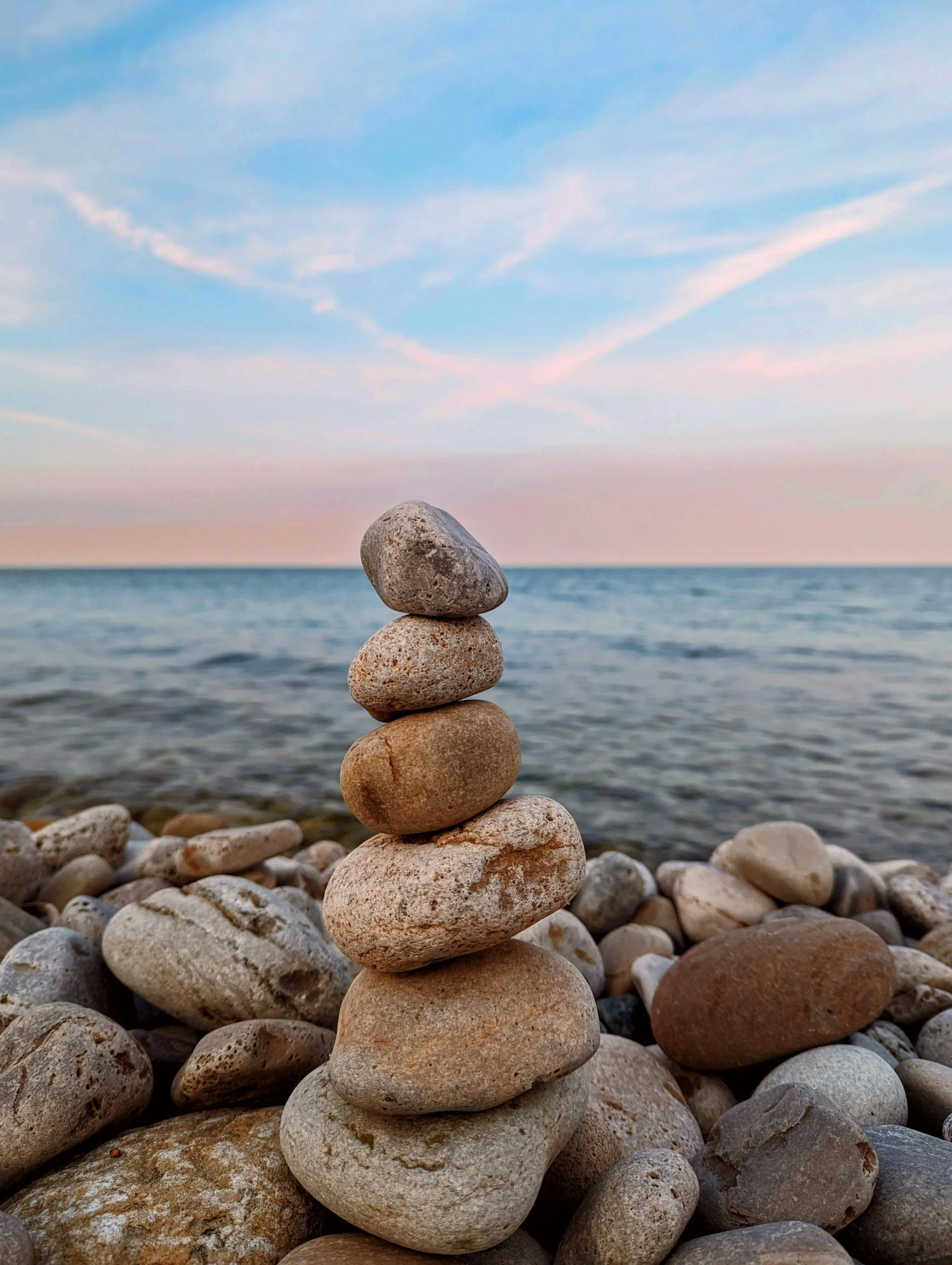 Aufeinander gestapelte Steine am Ufer eines ruhigen Gewässers bei Sonnenuntergang – Symbol für innere Balance, Achtsamkeit, emotionale Stabilität und persönliche Entwicklung.