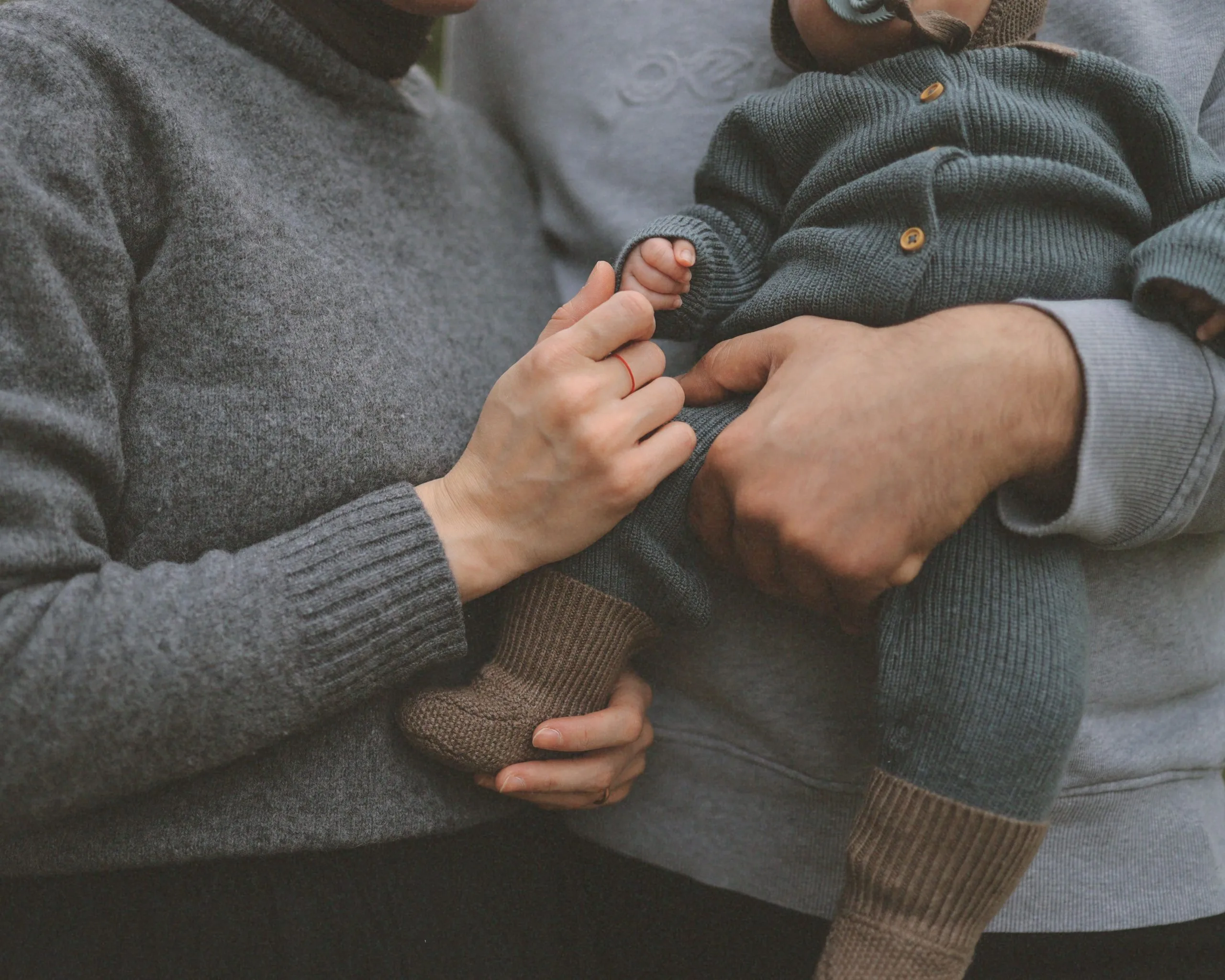 Eltern halten gemeinsam ihr Baby und berühren behutsam seine Hand – Symbolbild für die Beziehung nach der Geburt.