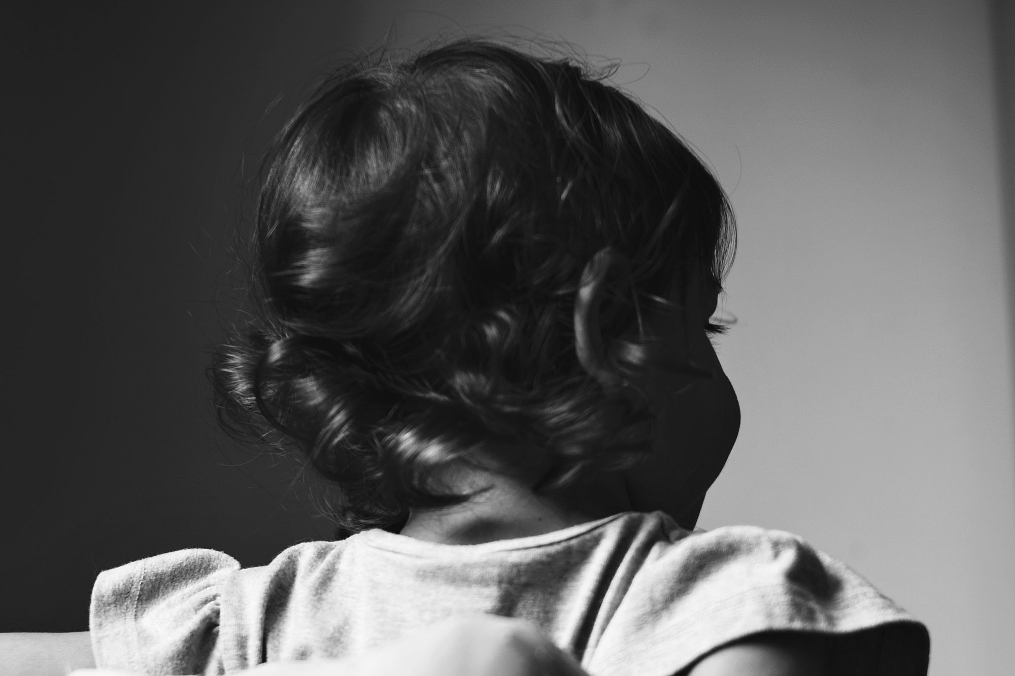 Streit nach der Geburt: Ein Kleinkind sitzt von hinten im Schatten und wirkt still und zurückgezogen.