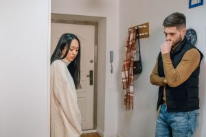 Beziehungsprobleme nach einem Streit: Eine Frau und ein Mann stehen mit Abstand im Flur, vermeiden Blickkontakt und wirken nachdenklich und emotional belastet.